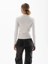 Polera blanca de tejido acanalado, con cuello alto y mangas largas ajustadas.