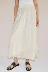 Falda midi fluida de tiro medio, color blanco, con cintura elástica ajustable mediante cordones y bajo asimétrico.