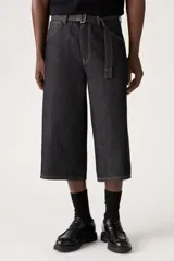 Pantalón capri de denim negro con corte amplio, tiro alto y cinturón de tela con hebilla metálica.