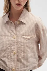 Chaqueta cropped de manga larga, color blanco con finas rayas verticales en tono claro. Presenta cuello camisa, cierre frontal con botones de madera y dos bolsillos delanteros con tapa a la altura del pecho.