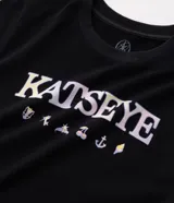 Remera negra de algodón con elastano, de corte ajustado, cuello redondo y mangas cortas. Presenta estampa frontal con la inscripción "KATSEYE" y pequeños símbolos gráficos en tono claro.