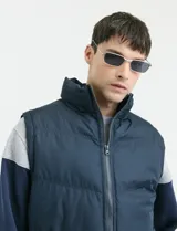 Chaleco capitoneado de color azul marino con cierre frontal completo y cuello alto. Presenta un diseño acolchado con costuras horizontales y forro interior con estampado escocés.