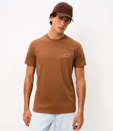 Remera marrón de manga corta con cuello redondo y corte comfort. Presenta una gran estampa en la espalda con diseño de paisaje playero, tablas de surf y tipografía, y estampa en el frente.