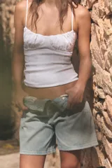 Top corsetero blanco de escote redondo con tirantes finos ajustables. Presenta detalles de frunces en el pecho y costuras verticales marcadas.