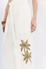 Pantalón blanco de algodón, tiro alto con corte paper bag y lazo a tono en la cintura. Presenta bordado de palmeras con lentejuelas y piedras en el lateral de la pierna.