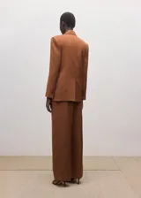 Pantalón de vestir estilo sastre color marrón, de corte recto, tiro bajo, con bolsillos laterales y cierre frontal de botón, gancho y cremallera.