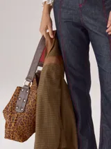 Cartera tipo hobo de cuero azul con textura granulada. Presenta un diseño holgado, con una correa de hombro bicolor que combina azul y rojo, sujeta por argollas metálicas. Incluye una placa metálica pequeña con el logo de la marca en la parte inferior frontal.
