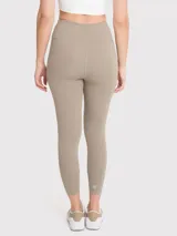 Calza deportiva de tiro alto con largo hasta el tobillo, confeccionada en tejido elástico de color beige. Presenta un diseño minimalista sin bolsillos y cuenta con un pequeño logo reflectante en la cadera.