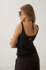 Top de punto negro con diseño acanalado vertical, escote redondo pronunciado y tirantes anchos con detalle de perlas o cuentas decorativas.
