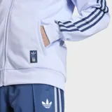 Campera deportiva Adidas Originals de la selección de Italia, color celeste con detalles en azul marino. Presenta cuello alto, cierre frontal, las icónicas tres tiras en las mangas, logo del Trifolio y escudo de la selección italiana en el pecho.