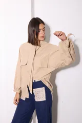Camisa de tela afelpada color beige con nudo en el cuello, mangas abullonadas con lazos en los puños y bolsillos frontales con tapa.