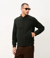 Campera bomber de hombre color verde oscuro, confeccionada en tejido polyvelour de textura aterciopelada. Presenta cuello, puños y cintura elastizados en ribana, cierre frontal oculto y bolsillos laterales.