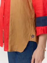 Camisa de lino color blanco con detalles combinados en tonos beige, cuello camisero, cierre frontal con botones oscuros y mangas largas con puños en contraste.