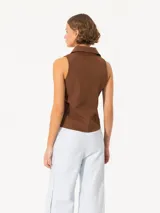 Camisa sin mangas confeccionada en tela de punto lisa, color crema, de corte regular. Lleva cartera con broches JCH y pinzas que entallan la prenda.