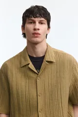 Camisa de manga corta H&M con cuello resort, cierre frontal de botones y bolsillos frontales aplicados. Confeccionada en tejido texturizado de corte relajado.