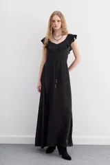 Vestido largo negro con escote pronunciado en V y volados que recorren el escote. Posee un cordón de ajuste en la cintura con terminaciones metálicas y falda amplia.