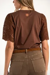 Remera de algodón peinado color negro, con mangas cortas de broderie con diseño calado y terminación festoneada. Presenta un corte oversize y cuello redondo.