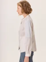 Camisa de algodón con diseño de bloques de color en tonos beige y gris claro, cuello mao, cierre frontal con botones y mangas largas con puños abotonados. Presenta costuras decorativas en contraste.