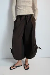 Pantalón culotte de tiro medio, color verde militar, con cintura elástica y bolsillos laterales ocultos. Presenta un diseño de bajo ancho con aberturas ajustables mediante cordones fruncidos en los laterales.