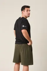 Bermuda deportiva color verde militar, de corte suelto, confeccionada en nylon. Cuenta con cintura elástica, cordón de ajuste, detalles de líneas en los costados y bolsillos con cierre.