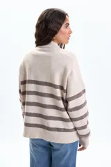 Buzo de tejido de punto con diseño a rayas horizontales en tonos beige y marrón. Presenta cuello redondo, mangas largas con puños acanalados y detalle de botones decorativos en uno de los hombros.