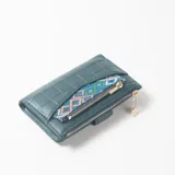 Billetera verde oscuro de cuero sintético con textura acolchada y bolsillo exterior con cierre y detalle de cinta étnica geométrica.