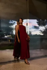 Vestido largo color burdeos con brillos, escote halter y espalda descubierta. El diseño es ajustado hasta la rodilla y se abre en una falda acampanada con vuelo.