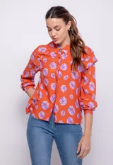 Camisa naranja con estampado de flores lilas, de manga larga con botones de plástico y detalle de alforzas en hombros.