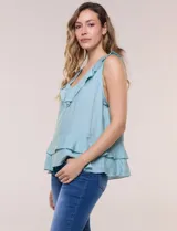 Blusa blanca sin mangas confeccionada en tejido de satén con suave textura arrugada y caída fluida. Cuenta con escote en V con volante en el cuello y ruedo estilo peplum con doble capa de volados superpuestos.