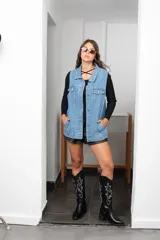 Chaleco de jean largo con corte oversize, cierre frontal con botones metálicos, bolsillos laterales y bolsillos superiores con solapa.