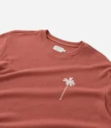 Remera de hombre color terracota, corte regular, cuello redondo y manga corta. Presenta un pequeño bordado de una palmera en el lado izquierdo del pecho.