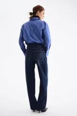 Jean de tiro alto y diseño barrel en denim de algodón azul, con corte de cinco bolsillos, cierre frontal con botón y cremallera, y piernas de corte curvo y holgado.