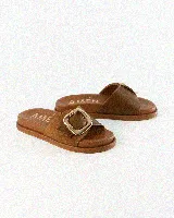 Sandalias de cuero color negro, de diseño plano con una tira ancha en el empeine y una hebilla metálica dorada grande como detalle.
