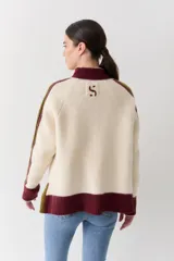 Campera de tejido de punto con cierre frontal, cuello alto y diseño color block en tonos marrón, rosa y rojo. Presenta detalles de trenzas en las mangas y puños y ruedo acanalados.