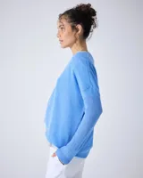 Sweater de punto fino color gris claro, con cuello en V y mangas largas. El tejido parece ser ligeramente transparente o muy liviano.