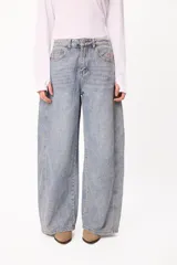 Jean de corte barrel con diseño de pierna ancha y tiro medio, confeccionado en denim de lavado claro. Presenta costuras laterales marcadas y un pequeño bordado del logo en el bolsillo delantero.