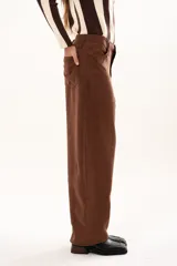 Pantalon de tiro medio con silueta curvada, mas ancha en la zona del muslo y la rodilla, con bolsillos laterales y cierre frontal con cremallera y boton.