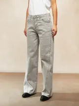 Jean de corte recto y tiro medio, confeccionado en denim de color gris lavado. Presenta costuras verticales decorativas con detalle de tachas a lo largo de las piernas y ruedo desflecado.