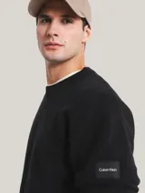 Sweater negro de lana y acrílico con cuello redondo, puños y bajo de canalé. Tiene una insignia con el logo de Calvin Klein en la manga.