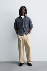 Camisa de algodón con estructura canvas, color rojo lavado, de corte relajado (relaxed fit) y manga corta. Posee cuello solapa, dos bolsillos de plastrón en el pecho y cierre frontal de botonadura. Presenta bordado y estampado de texto a contraste en el delantero.