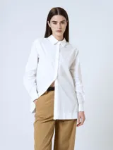 Camisa blanca de corte recto, con cuello clásico, cierre frontal con botones y mangas largas con puños abotonados.