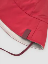 Sombrero tipo bucket reversible, con una cara en color rojo y otra en color gris. Cuenta con tiras ajustables para atar bajo la barbilla y etiqueta con logo en el lateral.