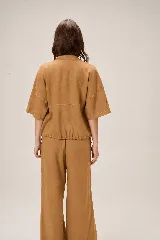 Chaqueta de lino y rayón color tostado, de corte holgado, mangas cortas amplias, cuello mao y cierre frontal oculto con cremallera. Presenta pespuntes a contratono en las costuras y cordón ajustable en el bajo.