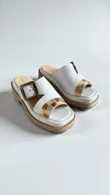 Sandalias de cuero natural blanco modelo Rina, con leve plataforma y suela dentada. Presentan una tira ancha cruzada con detalle pintado a mano multicolor y una hebilla metálica personalizada en tono oro viejo.