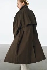 Trench oversize de Zara Woman Collection, confeccionado en mezcla de algodón con estampado de cuadros pequeños. Presenta cuello alto, cierre frontal con botones, mangas largas con trabillas ajustables y bolsillos laterales.