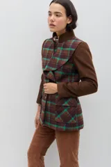 Chaqueta de lana en tono verde oliva con textura jaspeada, cuello mao y detalle de volado frontal. Presenta un corte entallado, bolsillos delanteros con solapa y cierre frontal con botones.