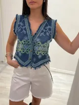 Chaleco corto en denim azul con detalle desflecado y bordado artesanal en tonos celeste y dorado. Estilo boho chic con escote en V, ideal para combinar con prendas básicas y elevar tu look.