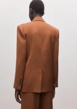 Blazer de corte sastrero color tostado, con diseño de doble botonadura, solapas clásicas y bolsillos laterales con solapa.