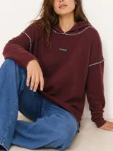 Sweater de punto color bordó con capucha, mangas largas, costuras externas en contraste con pespuntes y pequeño parche con logo de la marca en el pecho.