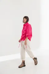 Camisa blanca de mangas largas con cuello clásico y cierre con botones. Presenta detalles de fruncido vertical en la parte delantera y cordones ajustables en los laterales. Corte holgado.